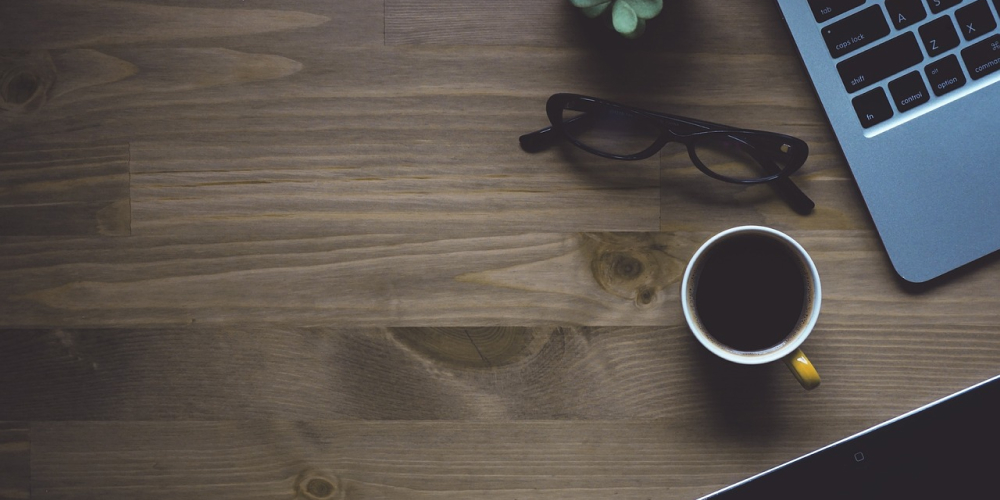 テーブルにコーヒーと眼鏡とパソコンがあります。作業中の様子です。